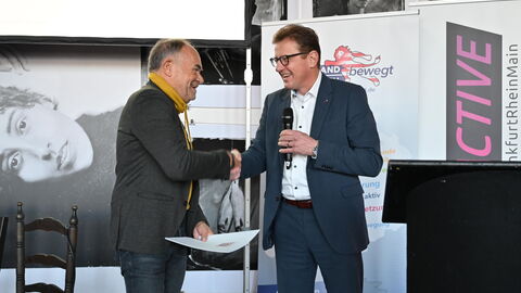 Stefan Sauer, Staatssekretär im Hessischen Innenministerium schüttelt dem Vorsitzenden des Sportkreises Frankfurt, Roland Frischkorn, bei der Übergabe des Förderbescheids die Hand