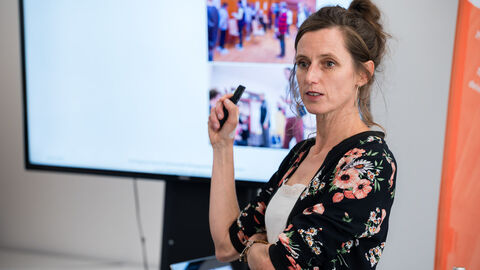 Fachforum 3: bewegt älter werden in der Kommune, Moderation (Evi Lindner) Evi Lindner bei der Moderation des dritten Fachforums: bewegt älter werden in der Kommune. Hinter ihr ist eine Flatscreen mit Präsentation zu sehen. Sie hält einen Pointer in der Hand.