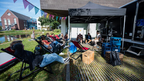 Bewegter Ausklang: Chill-out-area Man sieht das Außengelände (Parkanlage) vor dem Morgensternhaus, Es ist ein Pavillon aufgebaut. Davor und darunter stehen einige Liegestühle, in denen Personen sitzen. Rechts im Bild ist der Adventure-Cube der Sportjugend Hessen zu sehen. Es liegt einiges an Material rum (Boxen in verschiedenen Größen, Rucksäcke...)