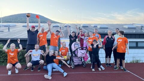 viele Menschen sins in zwei Reihen aufgestellt. Die hintere Reihe steht. In der vorderen Reihe hocken, sitzen oder stehen die Personen. Einige haben ein orangenes BeActive Shirt an. Viele Personen haben die Hände über die Köpfe gestreckt und sehen fröhlich aus. Auch ein Kinderwagen mit einem Kind darin steht in Mitten der Gruppe.