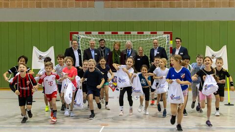 Teilnehmende Kinder des Bewegungschecks rennen in Sportkleidung lachend auf die Kamera zu. Im Hintergrund stehen u.a. Sportminister Peter Beuth, Staatssekretär im Kultusministerium Dr. Manuel Lösel, Bürgermeister der Gemeinde Buseck (Michael Ranft), Vizepräsidentin des lsb h (Katja Köhler-Nachtnebel), 1. Kreisbeigeordnete für Sport u. Schule (Christopher Lipp), Hauptgeschäftsführer der Barmer (Thorsten Noll), Vertreter des Schulamtes Gießen sowie Prof. Christopher Heim der Goethe-Universität Frankfurt