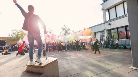 Step it up - Sport- und Musikfestival Mann steht auf Podest mit Mikrofon in der Hand und hebt die Hand in die Luft. Vor ihm stehen viele Menschen und werfen buntes Pulver in die Luft
