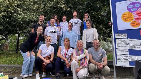 Mehrere Personen stehen und hocken in einer Gruppe vor Bäumen