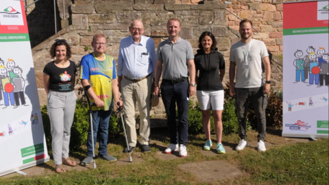 Aufgereihte Gruppe von Menschen im Freien, rechts und links stehen Roll-ups.