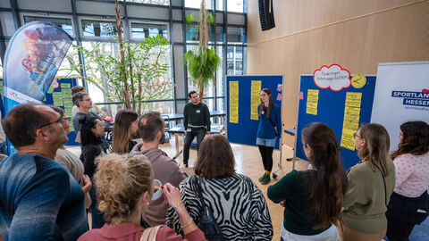Menschen stehen vor Pinnwand und hören Rednerin zu 