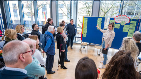 Menschen stehen vor Pinnwand und hören Rednerin zu 