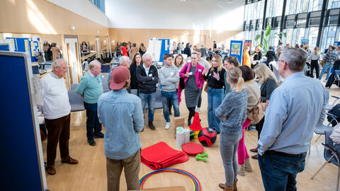 Eine Gruppe von Menschen stehen um eine Pinnwand und sprechen miteinander