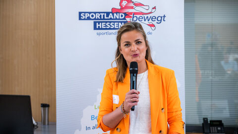 Frau mit Mikrofon in der Hand vor Roll-up des Landesprogramms