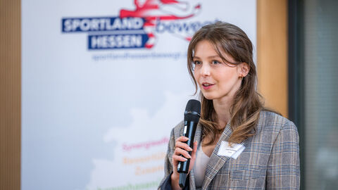 Frau mit Handmikrofon vor Roll-up des Landesprogramms