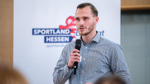 Mann mit Mikrofon in der Hand vor Roll-up