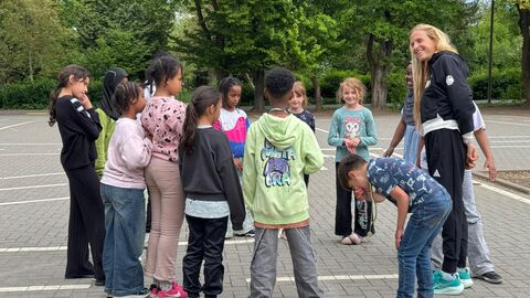 Laura Hottenrott zu Besuch an der Leinius-Schule Kinder und eine Erwachsene Person stehen in einem Kreis auf einem Schulhof.