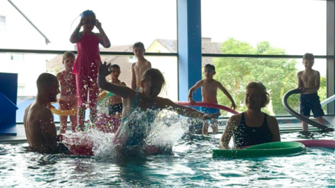 Kinder springen im Hallenbad vom Beckenrand.