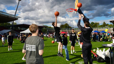 Menschen spielen Basketba mit Korb auf Wiese.
