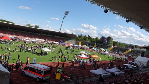 Stadionrasen mit vielen Menschen und Pavillions